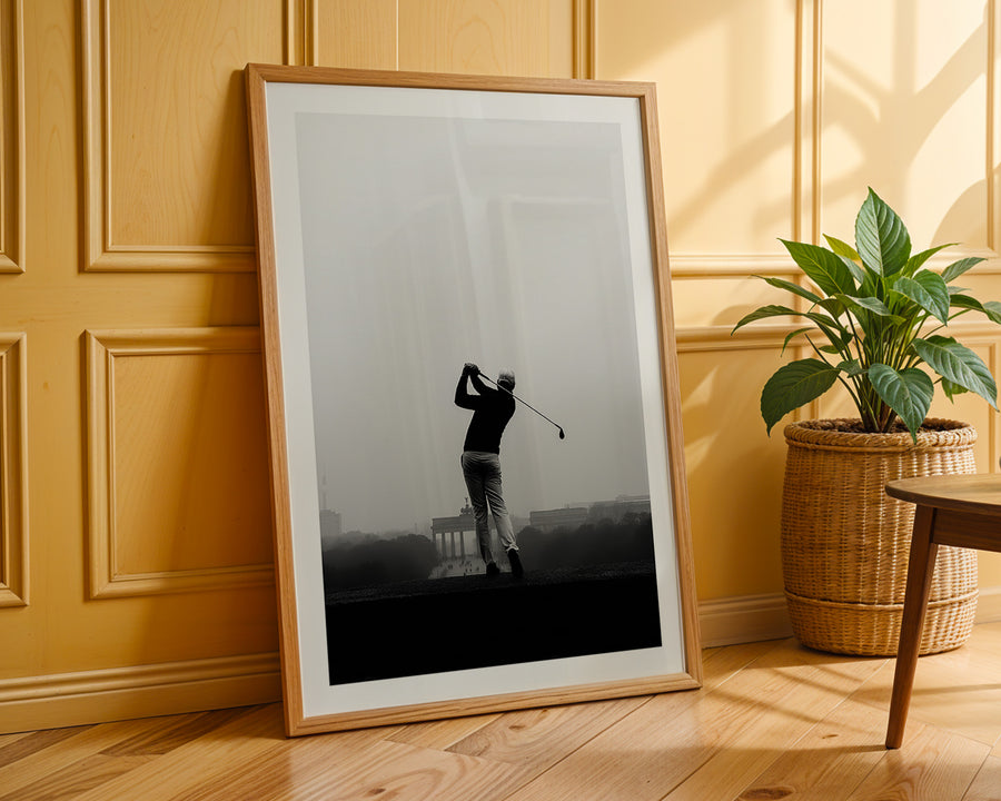 Framed black and white print of a golfer on a wooden floor with a plant in the background