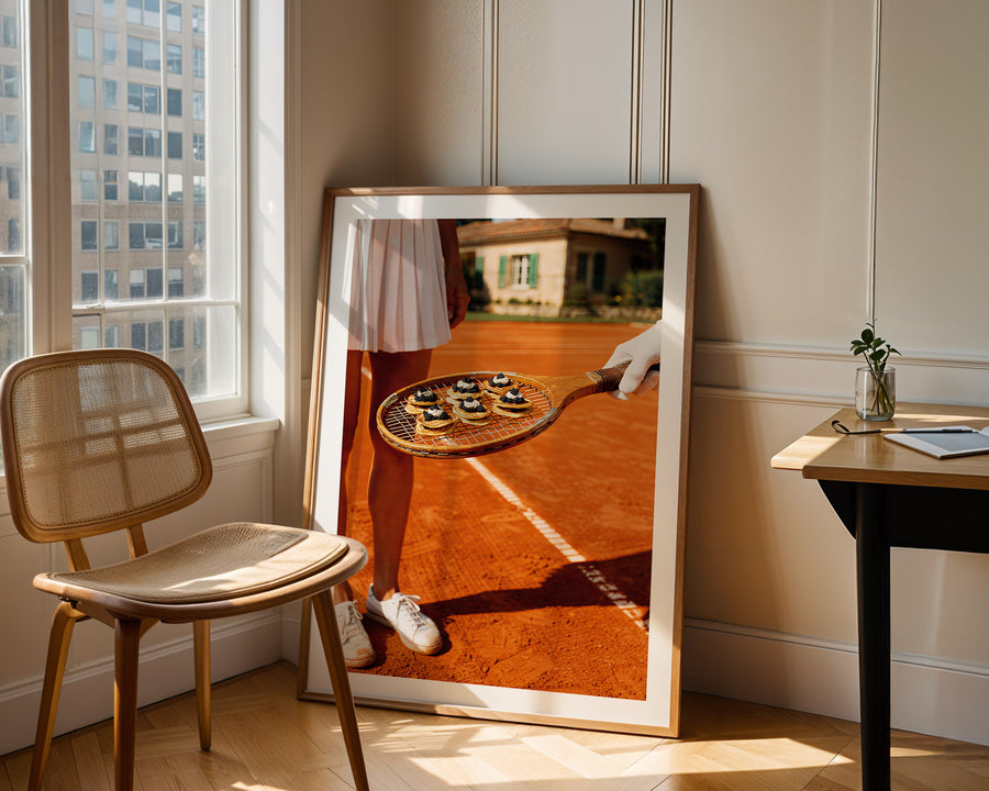 Framed artwork of a person holding a tennis racket with a ball on a wooden floor, leaning against a wall.