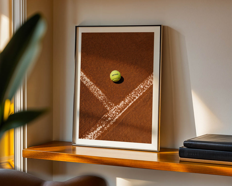 Framed picture of a tennis ball on a tennis court with a plant and books in the background