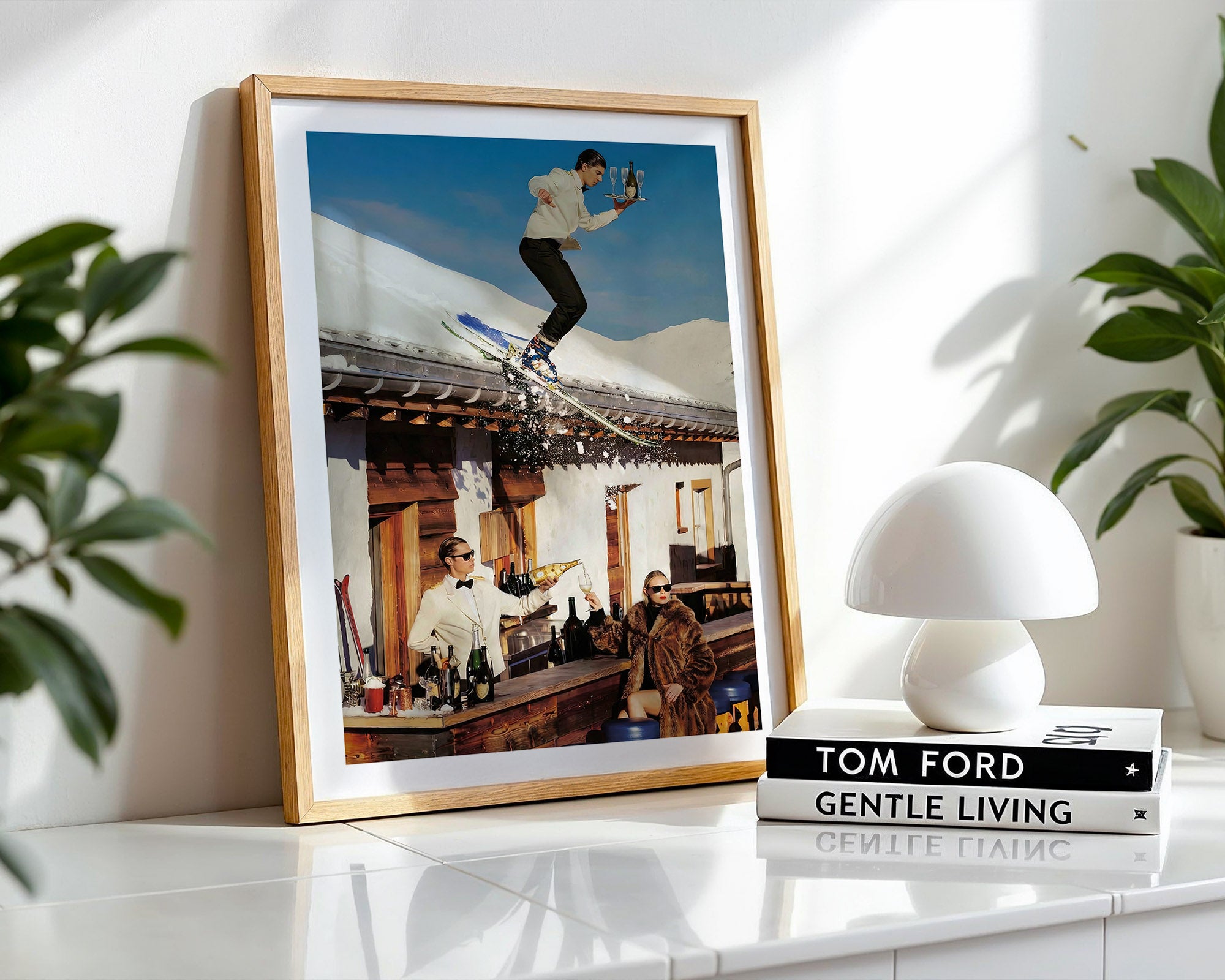 Framed photo of a man skiing with champagne on a rooftop with a white lamp and books on a shelf.