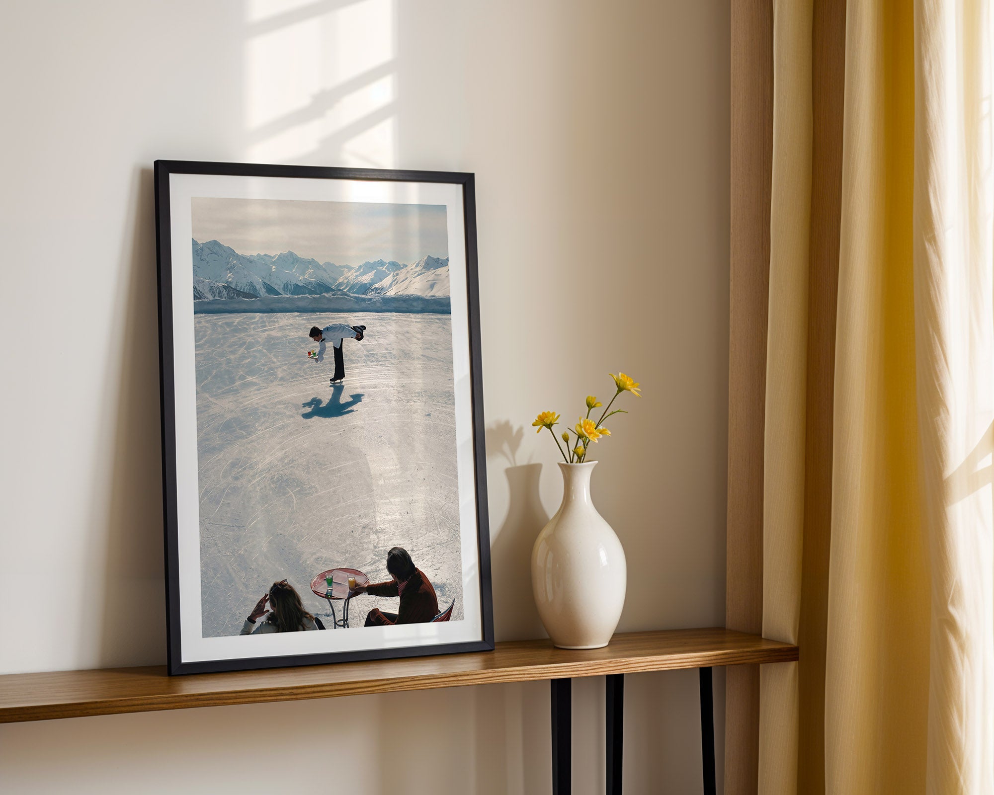 Framed artwork on a wooden shelf with a vase and flowers against a light wall.