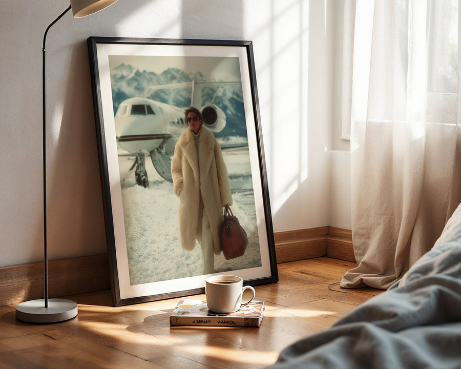 Framed photograph of a person in a coat standing next to an airplane on a wooden floor with a lamp and book in the foreground.