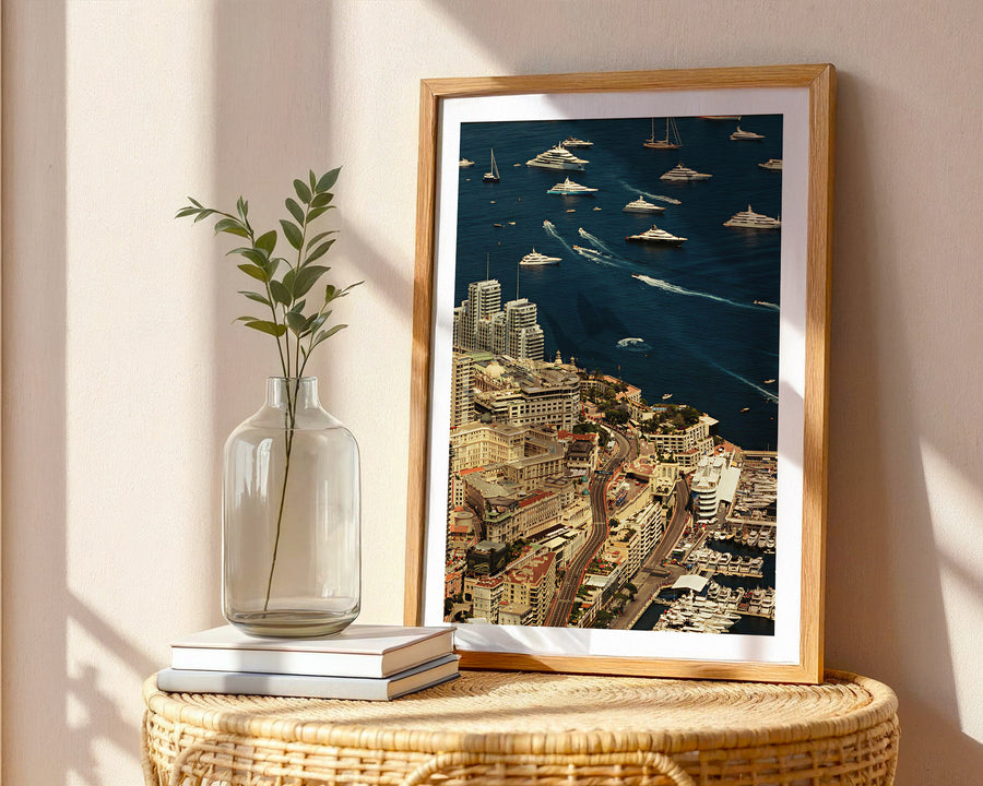 Framed cityscape print on a wall next to a vase with a plant and books.