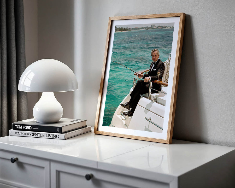 Framed photograph of a man on a boat next to a white lamp and books on a shelf.
