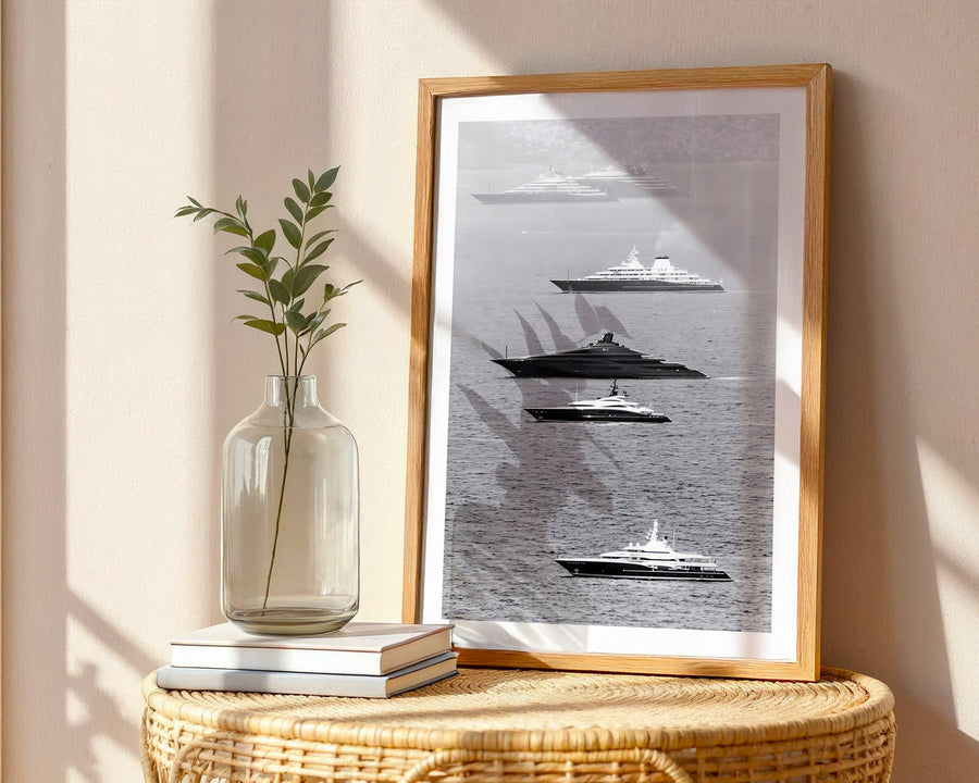 Framed black and white nautical art on a wall with a vase and books on a table.