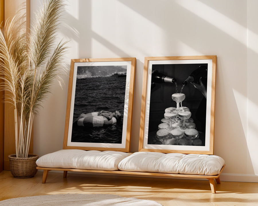 Two framed black and white artworks on a wooden bench with a plant in the background.