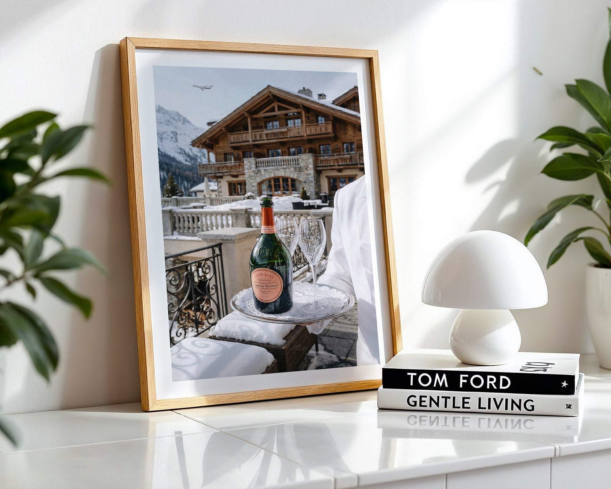 Framed photograph of a snowy mountain scene with a bottle of champagne on a table.