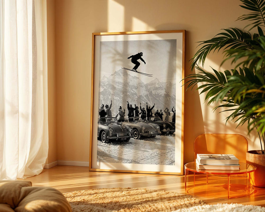 Framed black and white photo of a skier in mid-air over vintage cars in a living room.