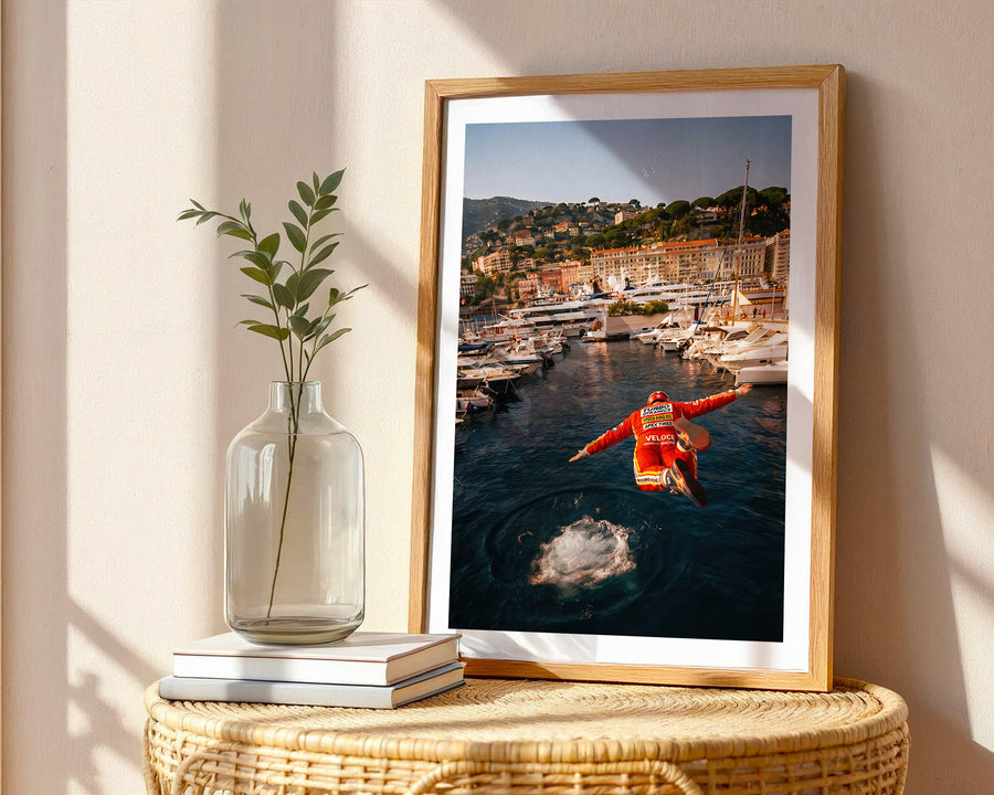 Framed photograph of a person in an orange jacket on a dock with a scenic view, placed on a wicker table with a vase and books.