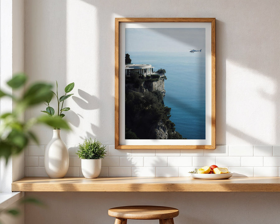 Framed artwork of a coastal scene with a boat, displayed on a wall above a wooden shelf.