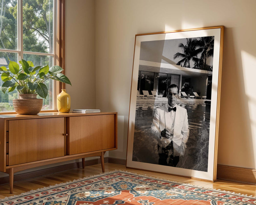 Framed black and white portrait of a man in a stylish outfit leaning against a wall in a room with a wooden sideboard and decorative rug.