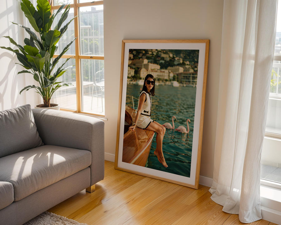Framed photograph of a woman on a boat in a living room with a gray sofa and large window.