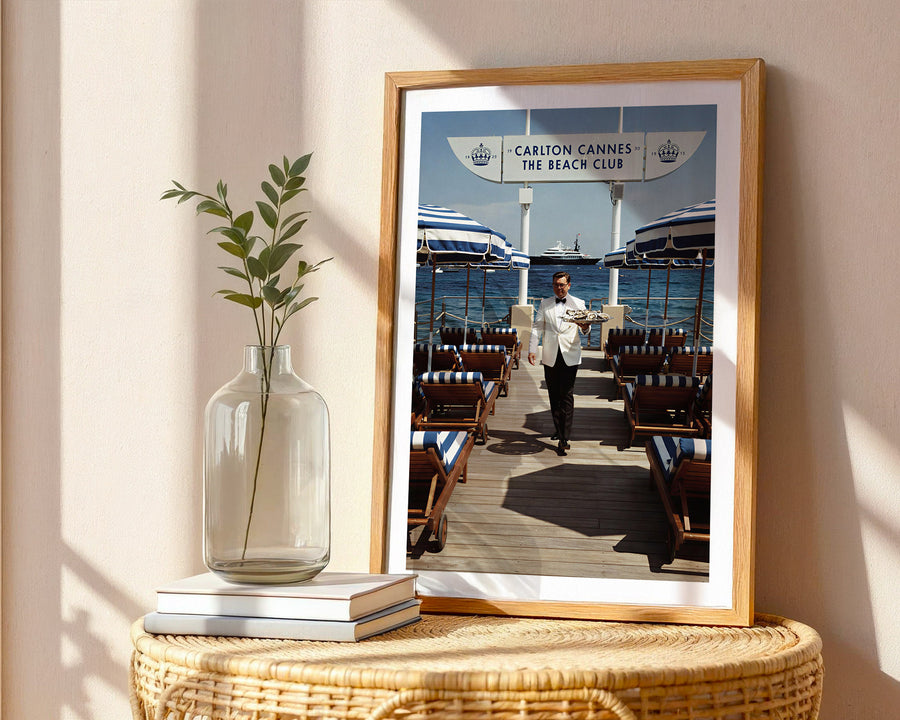 Framed photograph of a beach club scene with a vase and books on a table.