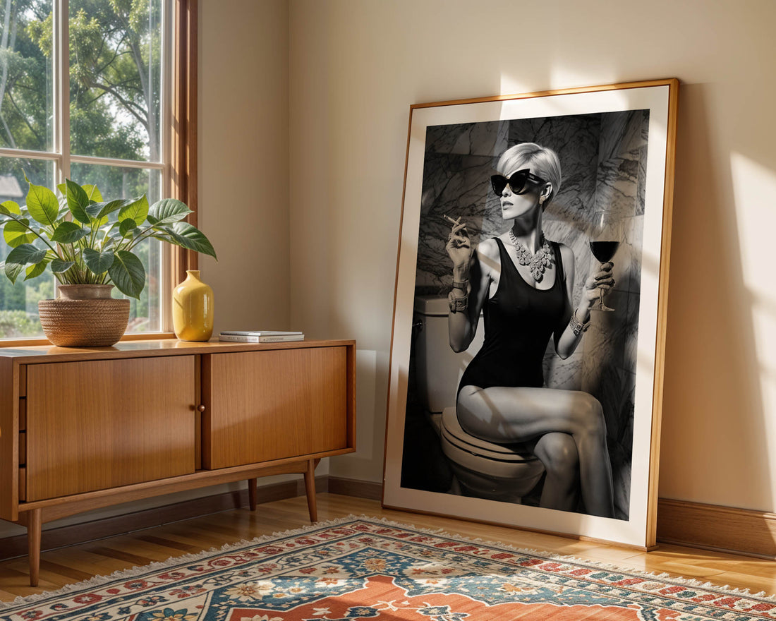Framed artwork of a woman sitting on a toilet in a room with a wooden cabinet and decorative rug.