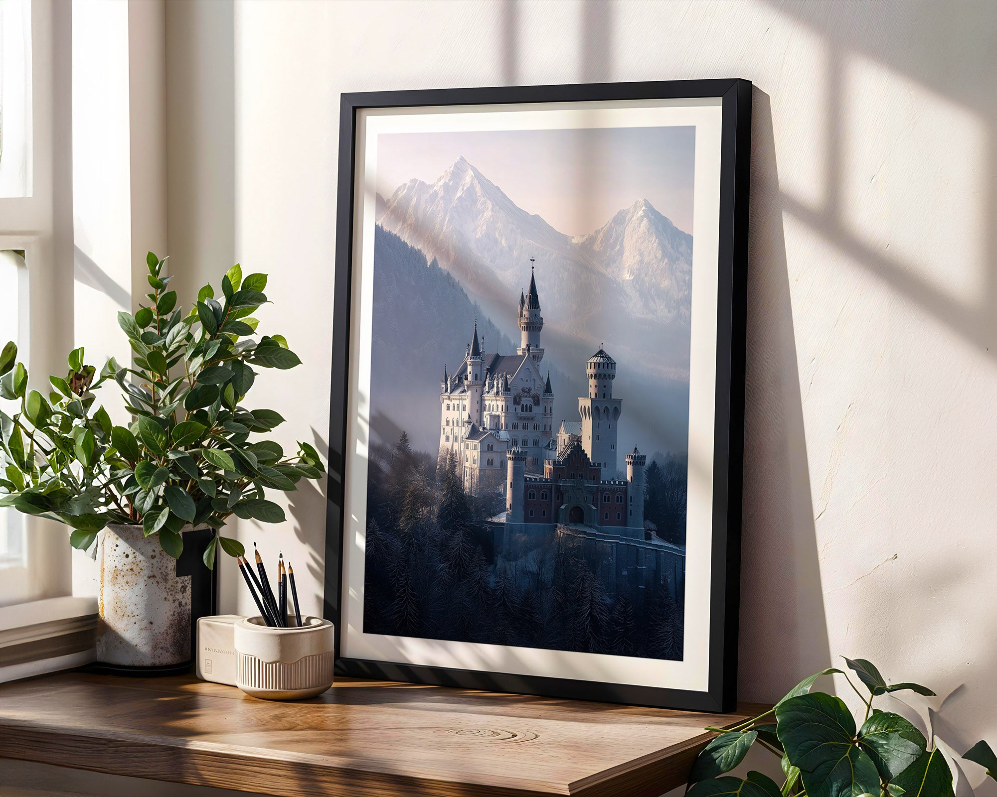 Framed artwork of a castle in the mountains on a wooden shelf with plants.