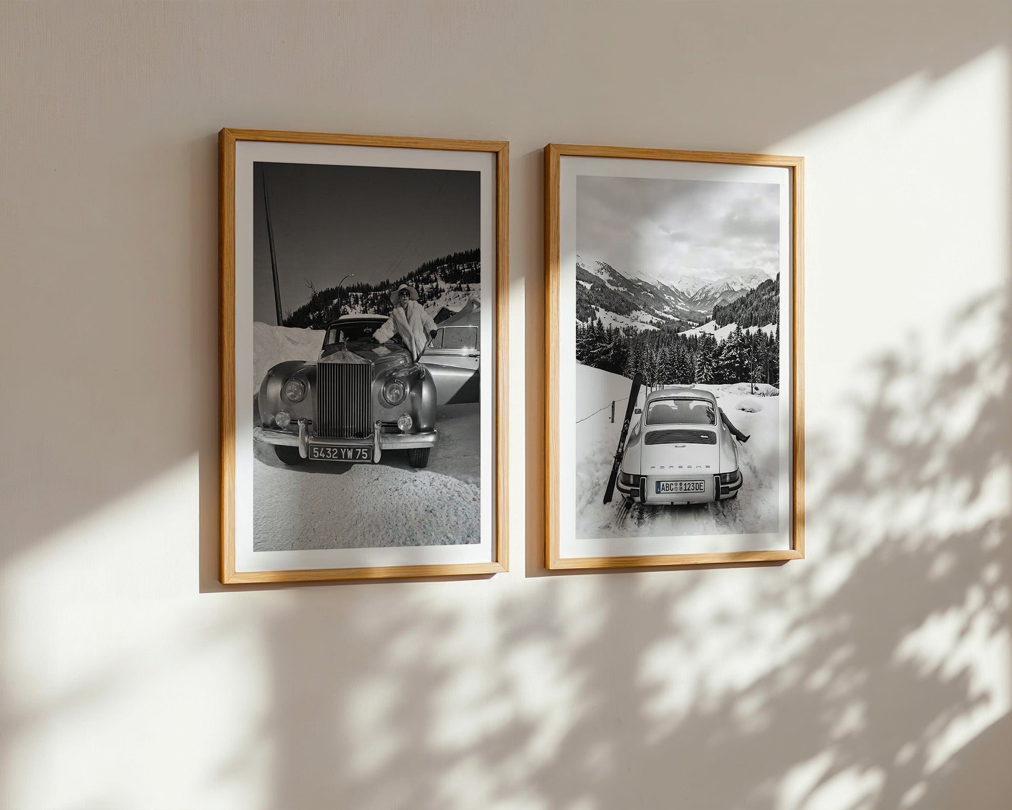 Two framed black and white photographs of vintage cars on a wall with sunlight casting shadows.