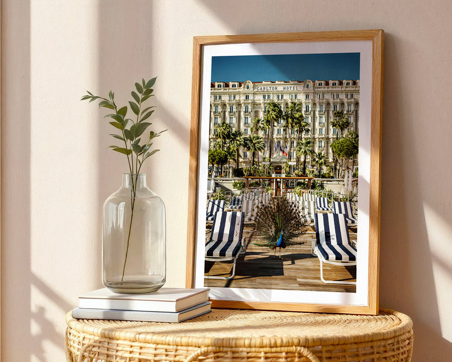 Framed photograph of a beach scene with palm trees and buildings, placed on a wicker table with a vase and books.
