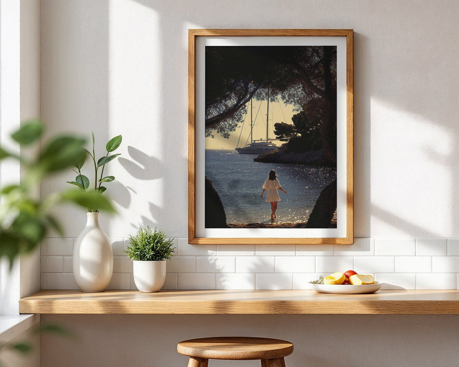 Framed artwork of a woman by a lake with sailboats, displayed on a wall above a wooden shelf.