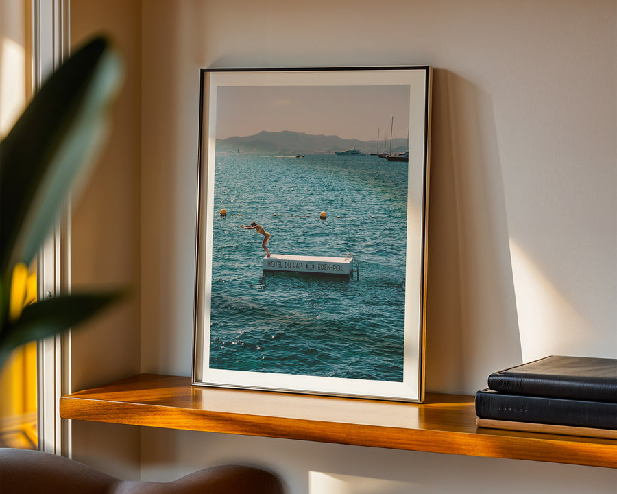Framed photograph of a beach scene on a wooden shelf with books.
