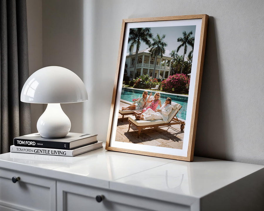 Framed photograph of a family by a pool on a white surface with a lamp and books.