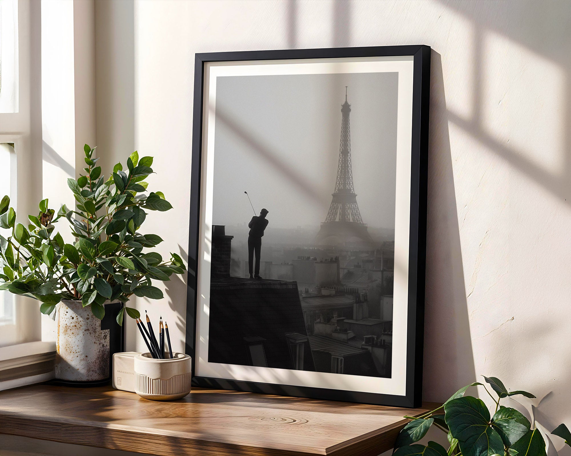Framed black and white artwork of a cityscape with a silhouette of a person on a windowsill.