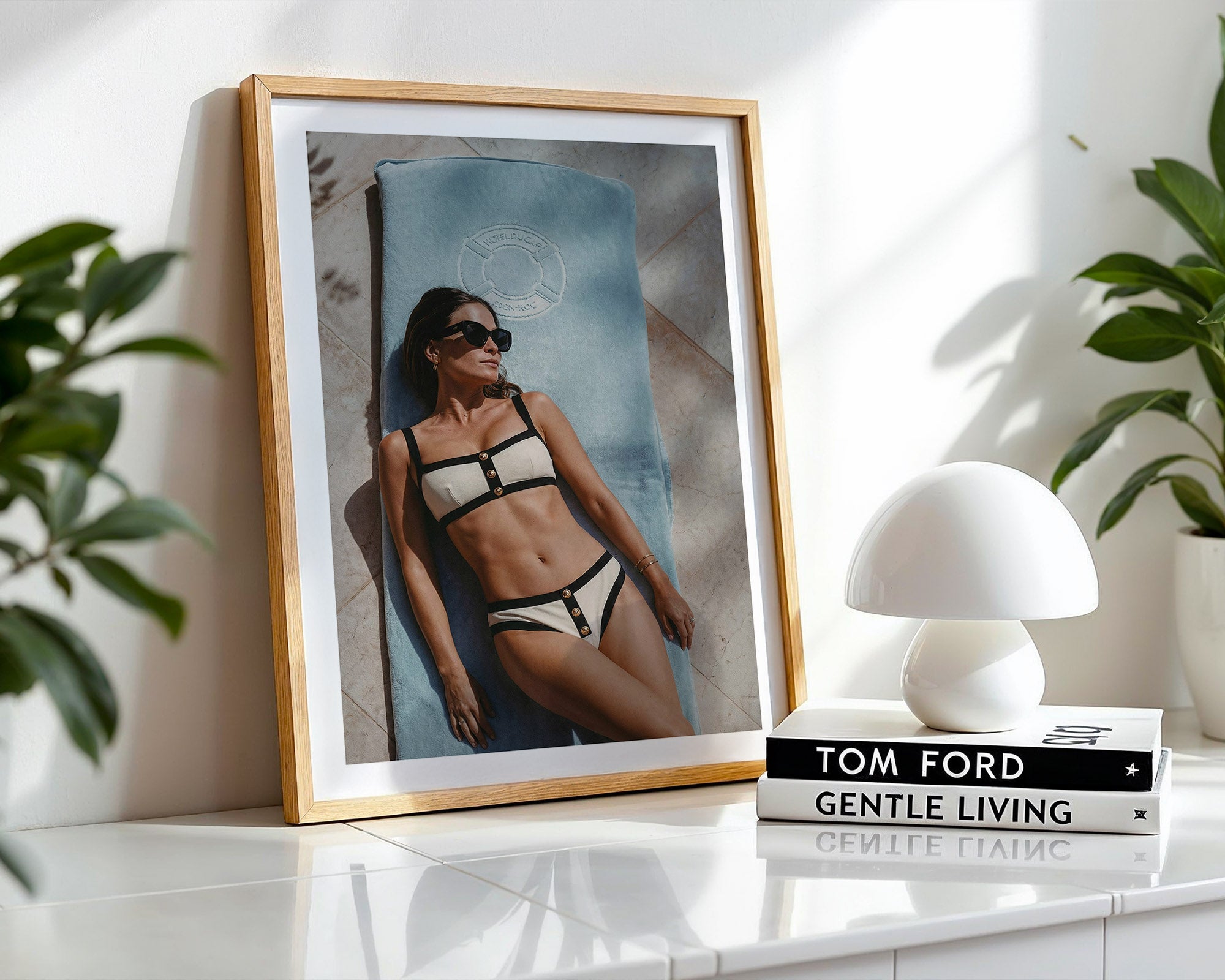 Framed photo of a woman in a Chanel bikini on a shelf with a white lamp and 'Tom Ford Gentle Living' book.