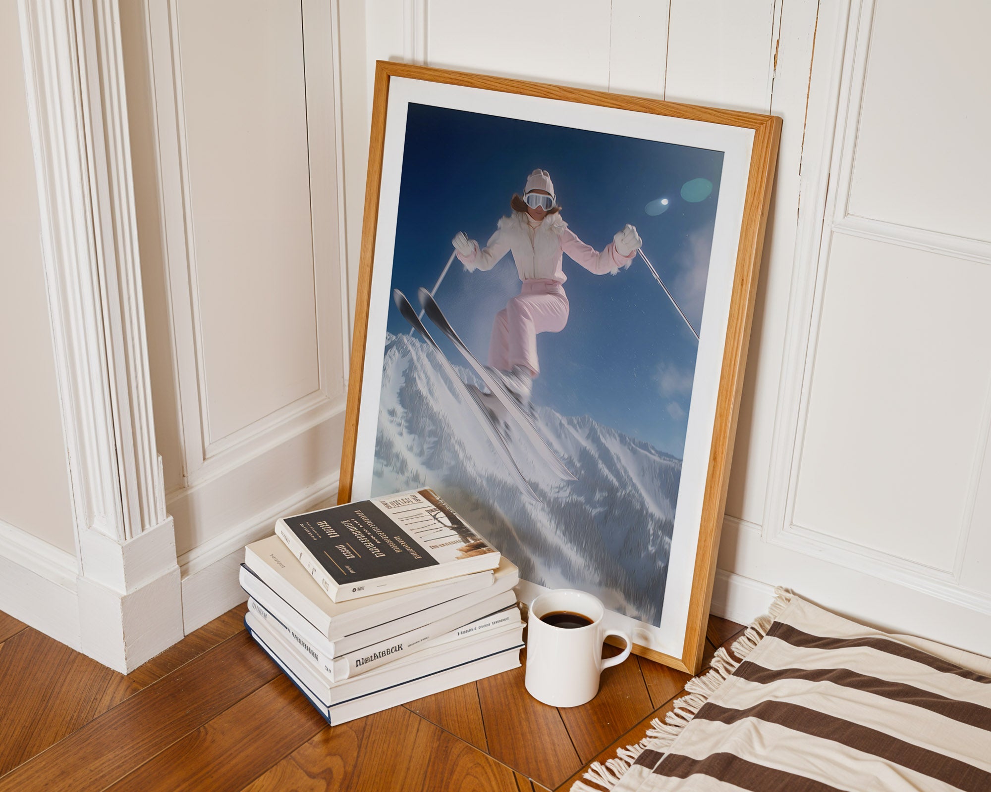 Framed photograph of a skier on a mountain next to books and a mug on a wooden floor.