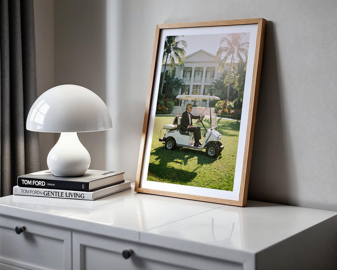 Framed picture of a man on a golf cart on a dresser with a lamp and books.
