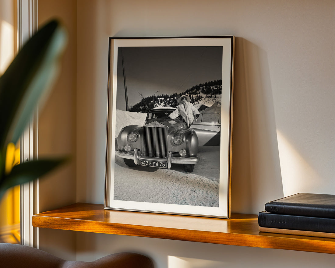 Framed black and white photograph of a vintage Rolls-Royce on a shelf with books and a plant.