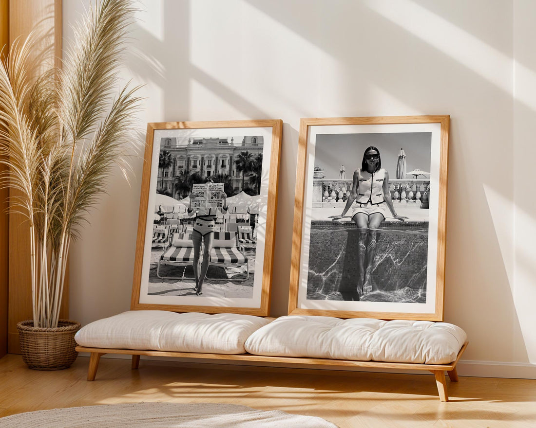 Two framed black and white photos on a wooden bench with a plant in the background.