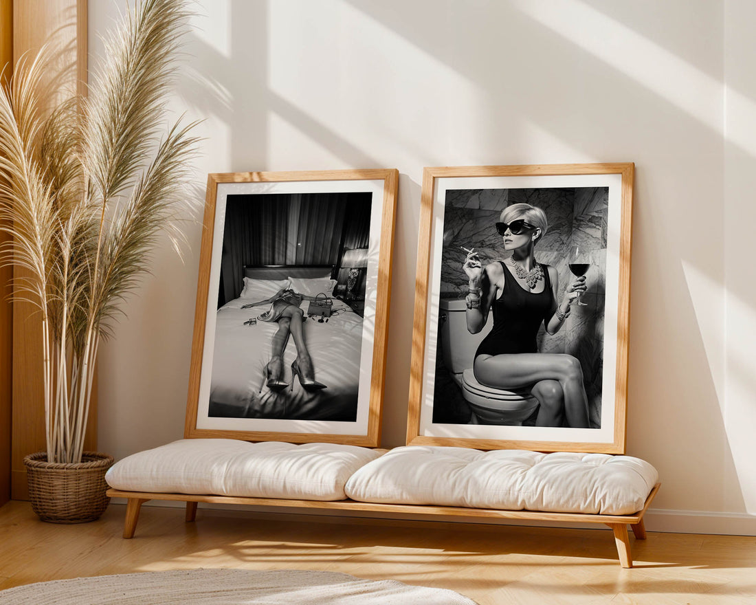 Two framed black and white artworks on a wall with a plant and bench in the foreground.