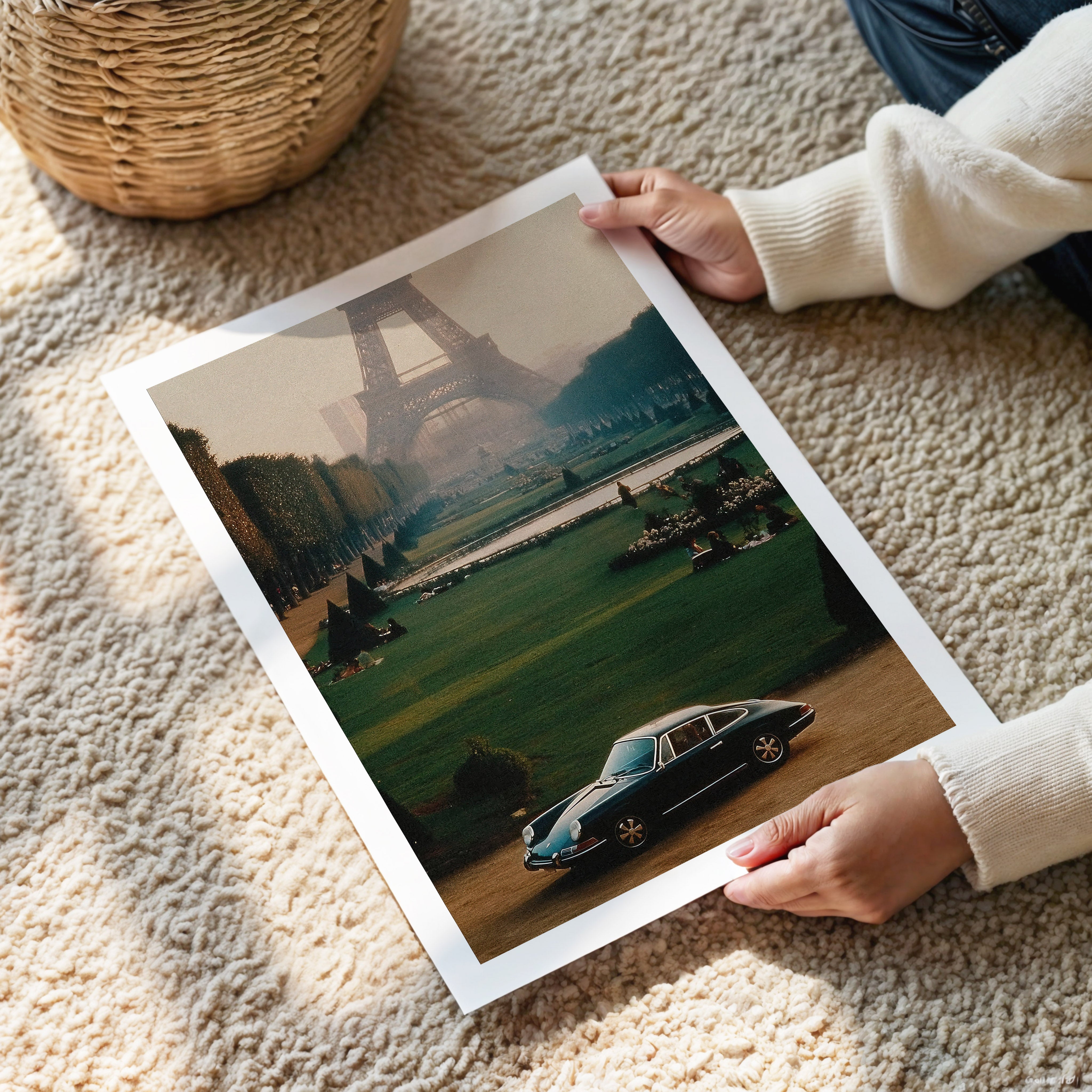 Person holding a framed print of a car and Eiffel Tower in Paris on a carpeted floor.