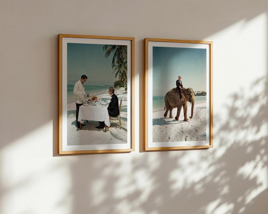 Two framed photographs on a wall showing a beach scene with people and an elephant.