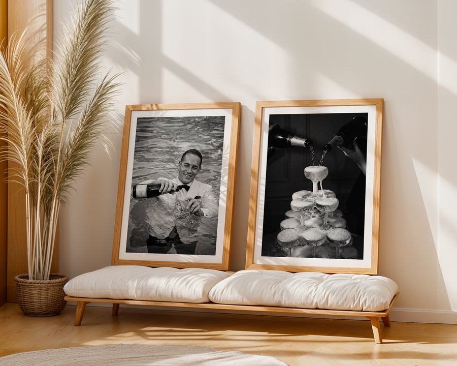 Two framed black and white photos on a wooden bench with a plant in the background.