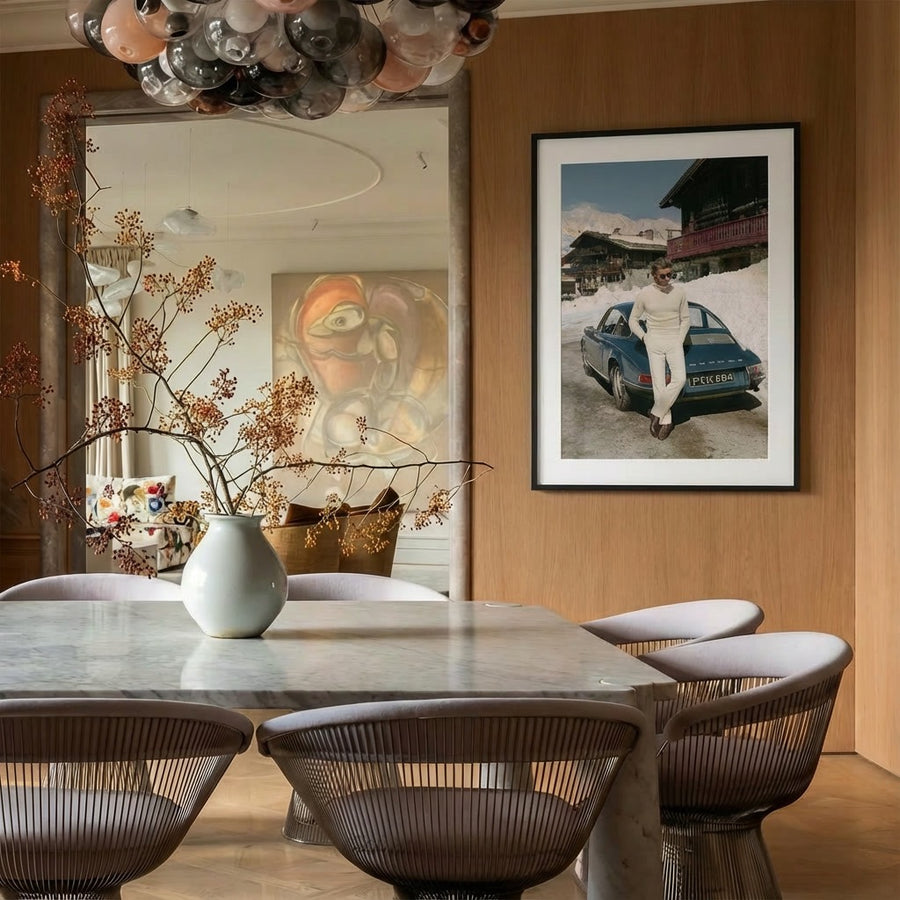 Dining room with marble table, chairs, and wall art of a person with a car in the snow.