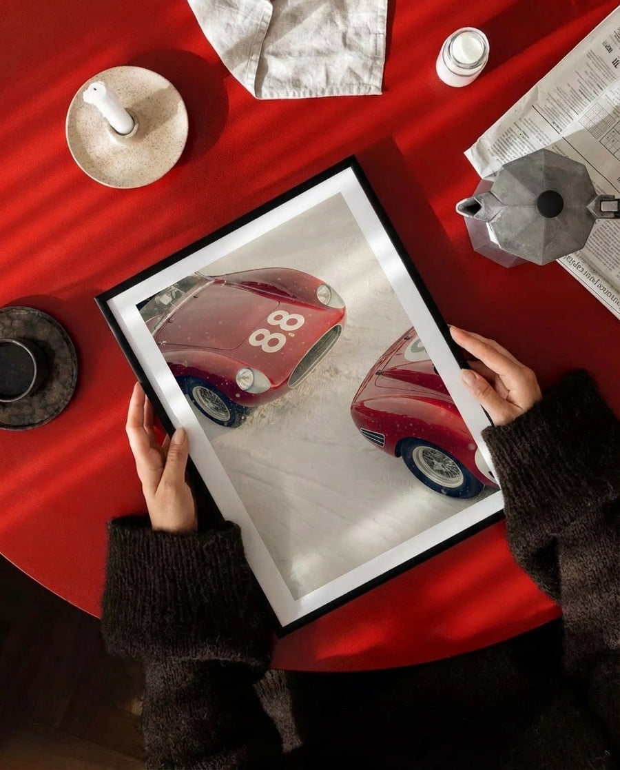 Person holding a framed picture of a red car with the number 88 on a red table.