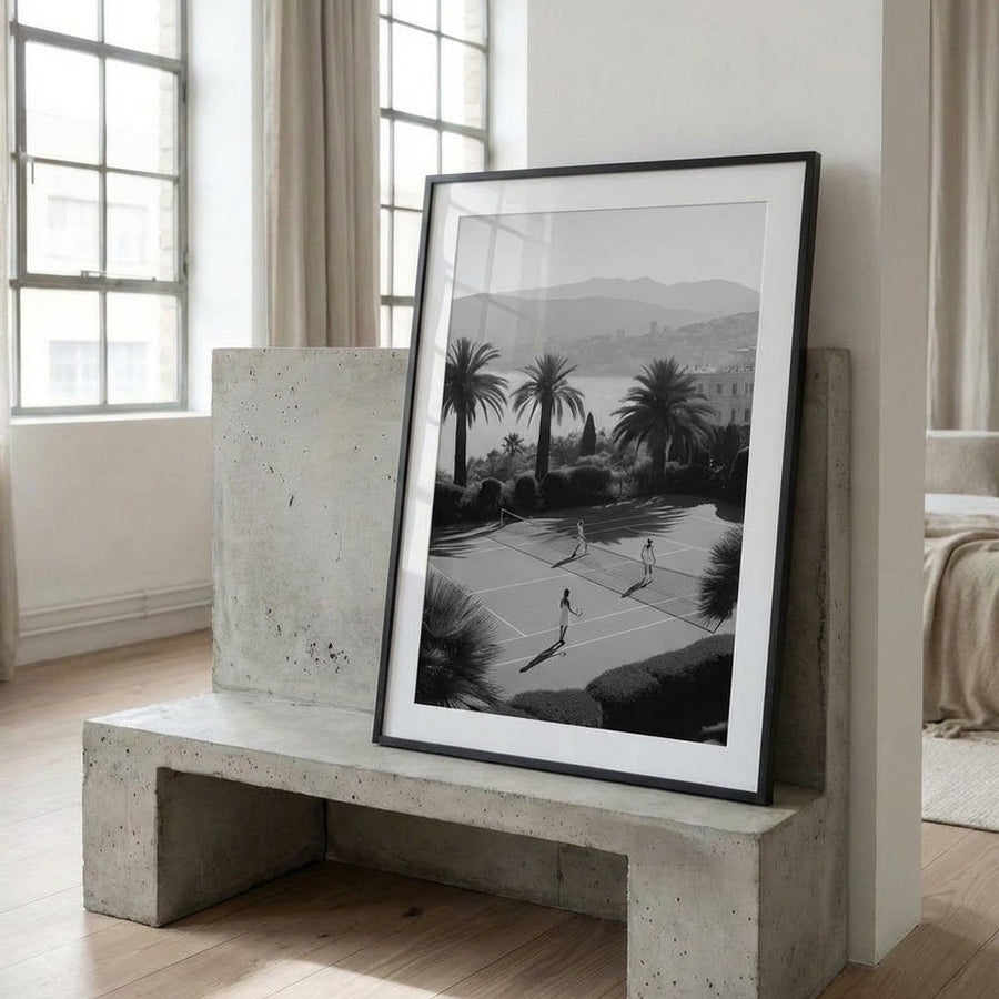Framed black and white artwork on a concrete bench in a room with large windows.