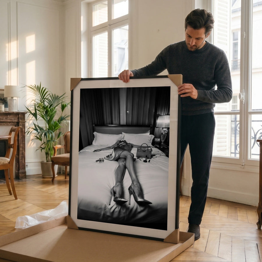 Man holding a framed black and white photograph in a room with large windows.