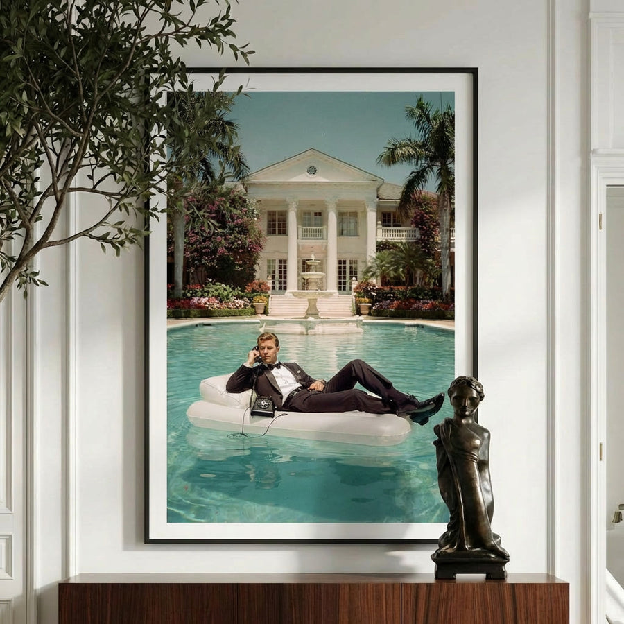 Framed photograph of a man on an inflatable pool float by a pool with a large house in the background, displayed on a wall.