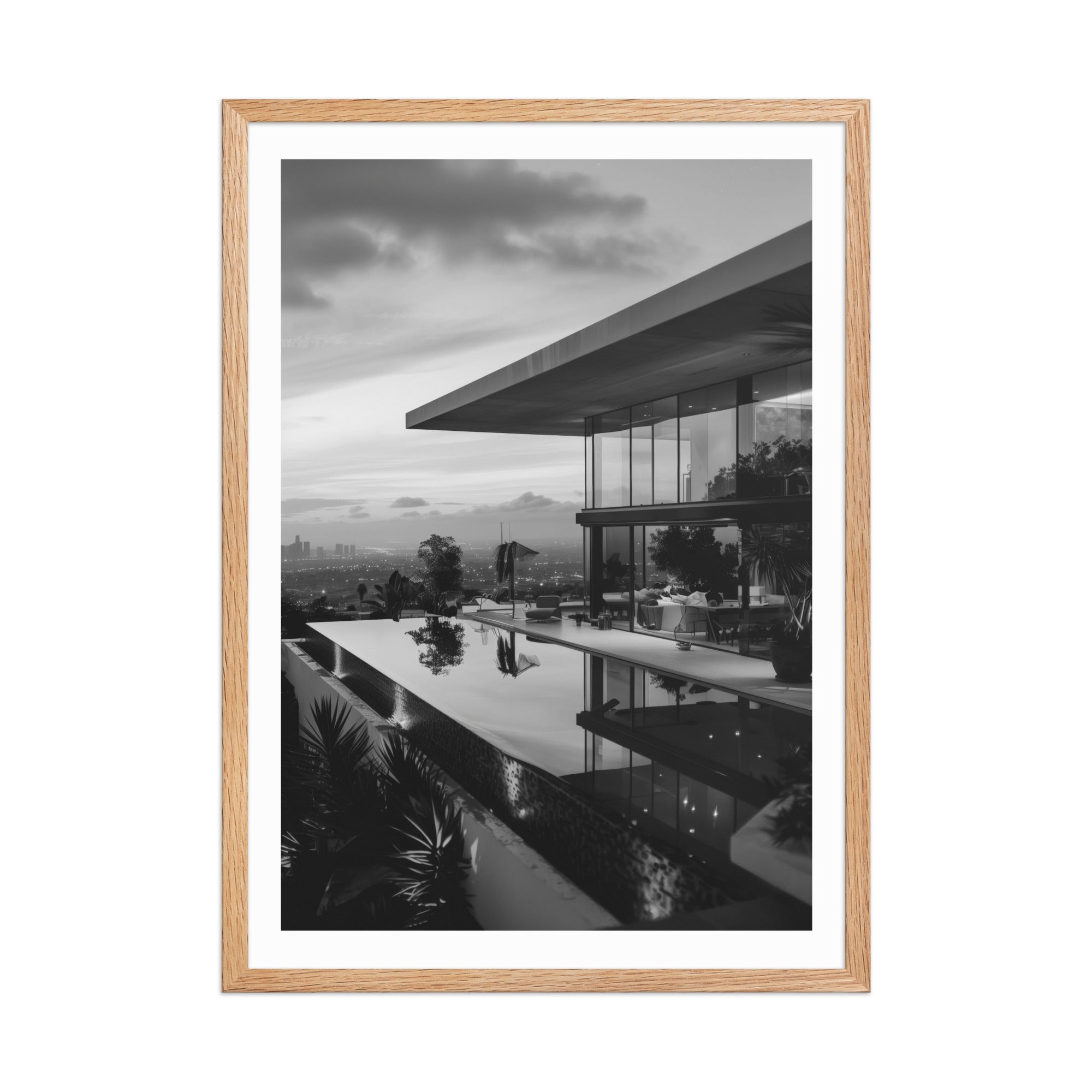 A framed black and white architectural photograph of a modern house with an infinity pool, presented in a light natural wood frame with a white mat, on a solid white background.