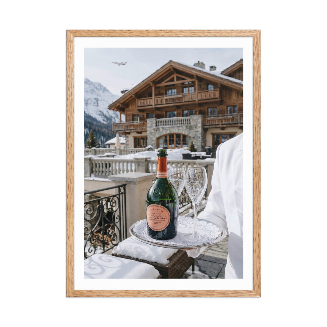 Framed photograph of a bottle of champagne and glasses on a tray with a snowy mountain cabin in the background.