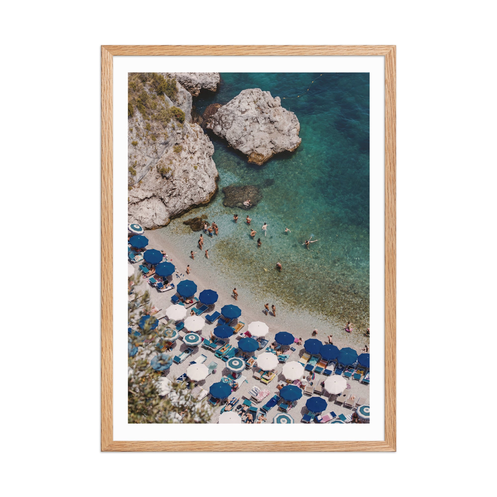 Framed artwork of a beach scene with blue umbrellas and people near rocky cliffs.