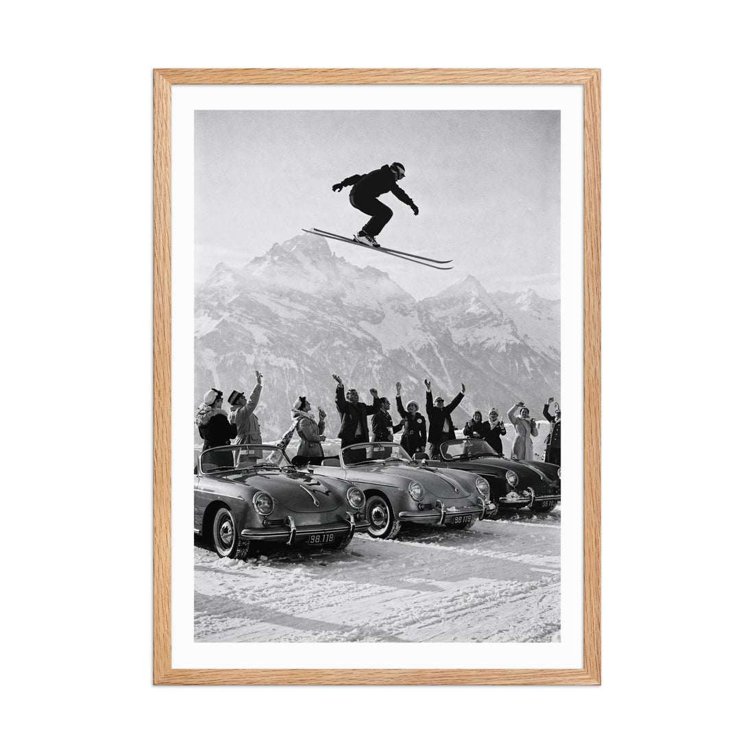 Framed black and white poster of a skier jumping over cars with a mountain background