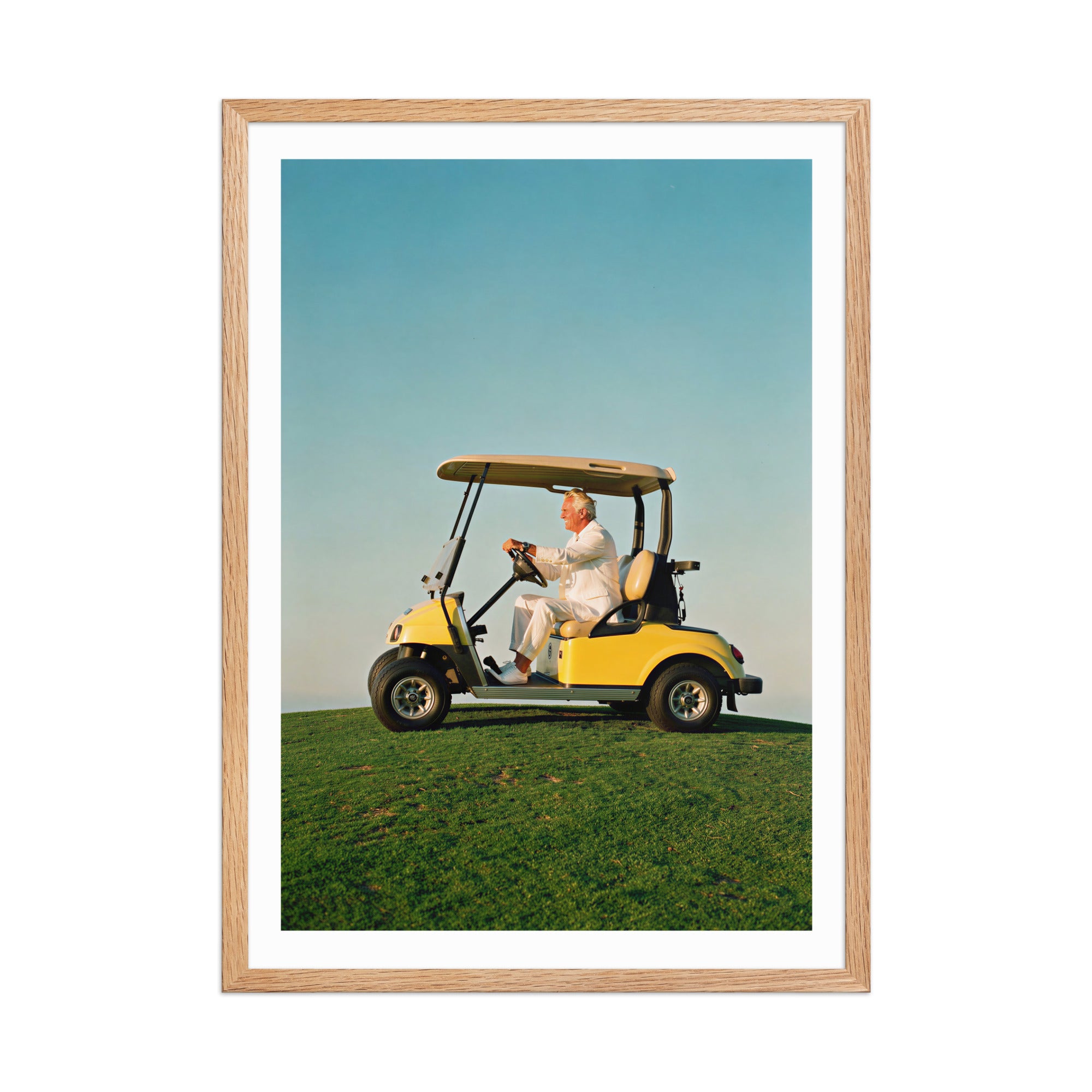 Framed photograph of a person in a yellow golf cart on a grassy field with a clear blue sky.