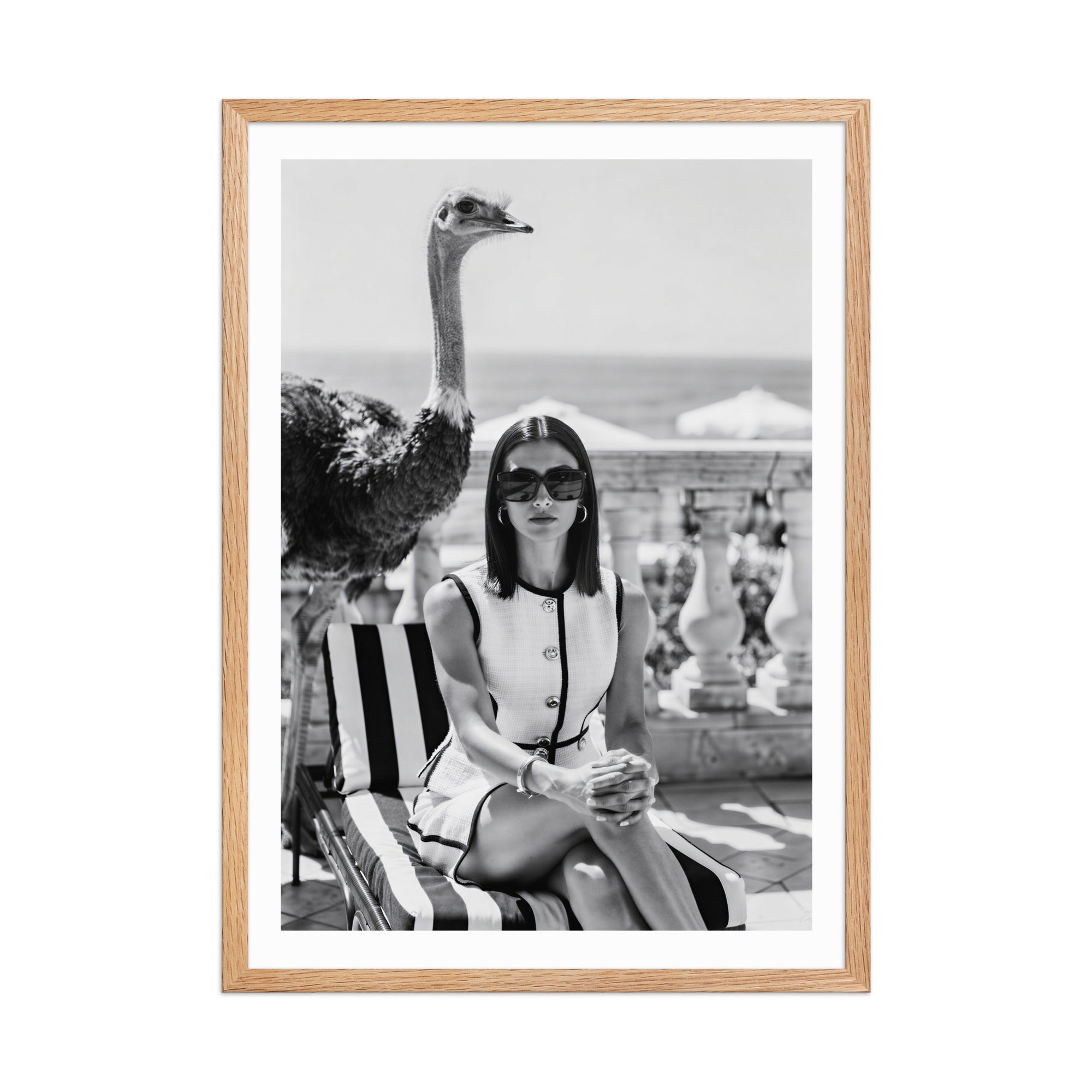 Framed black and white photo of a woman sitting on a striped chair with an ostrich.