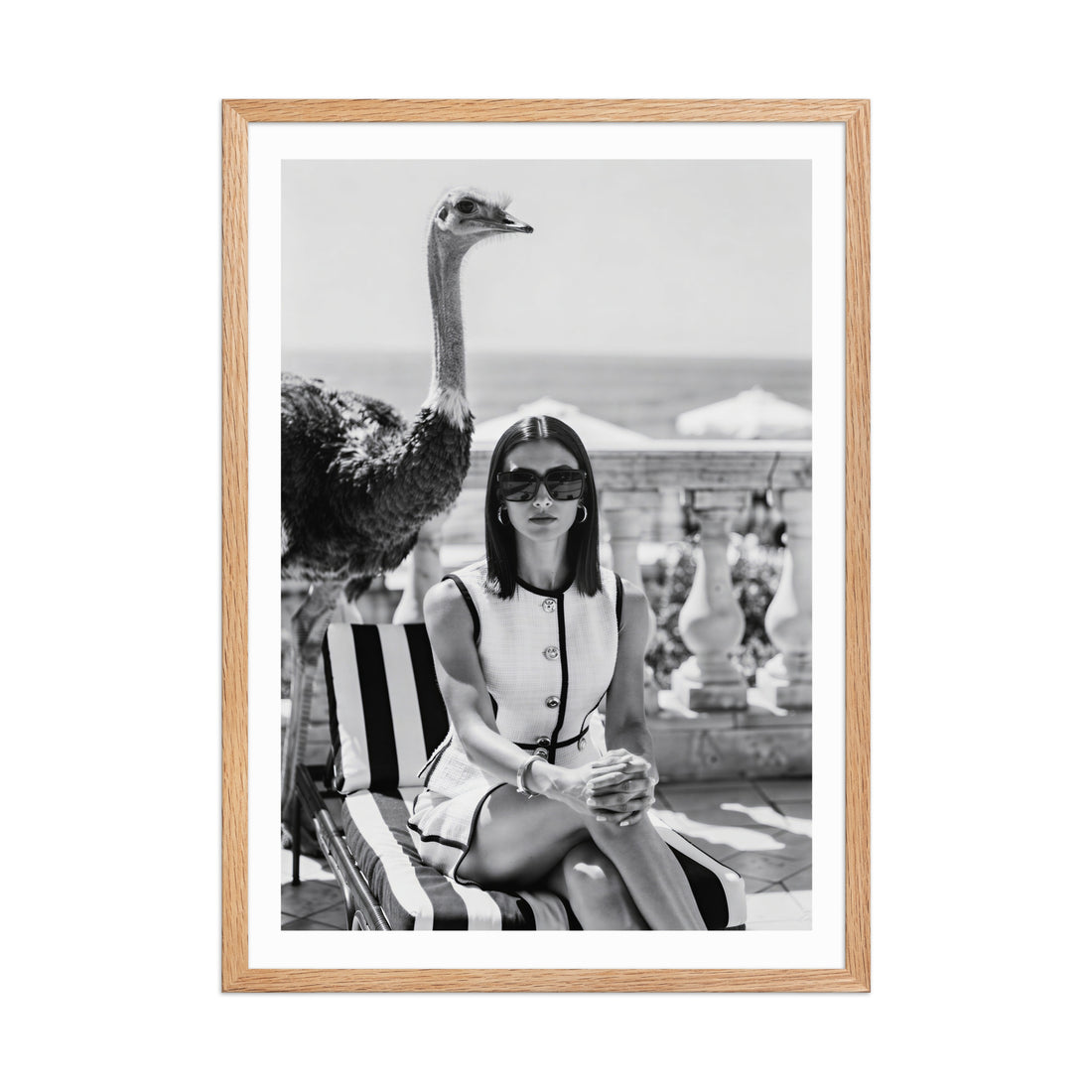 Framed black and white photo of a woman sitting on a striped chair with an ostrich.