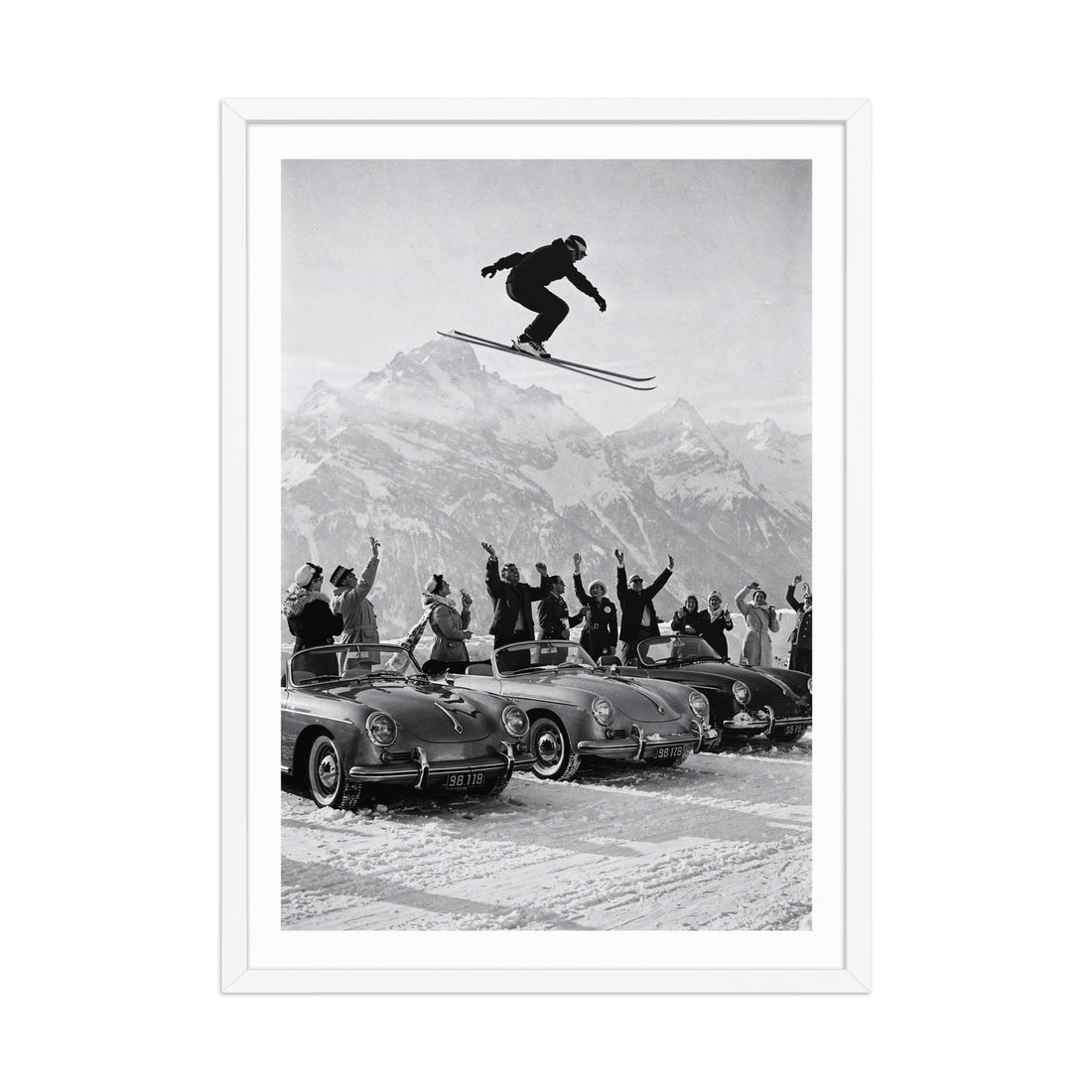 Framed black and white print of a skier jumping over cars with a mountainous background.