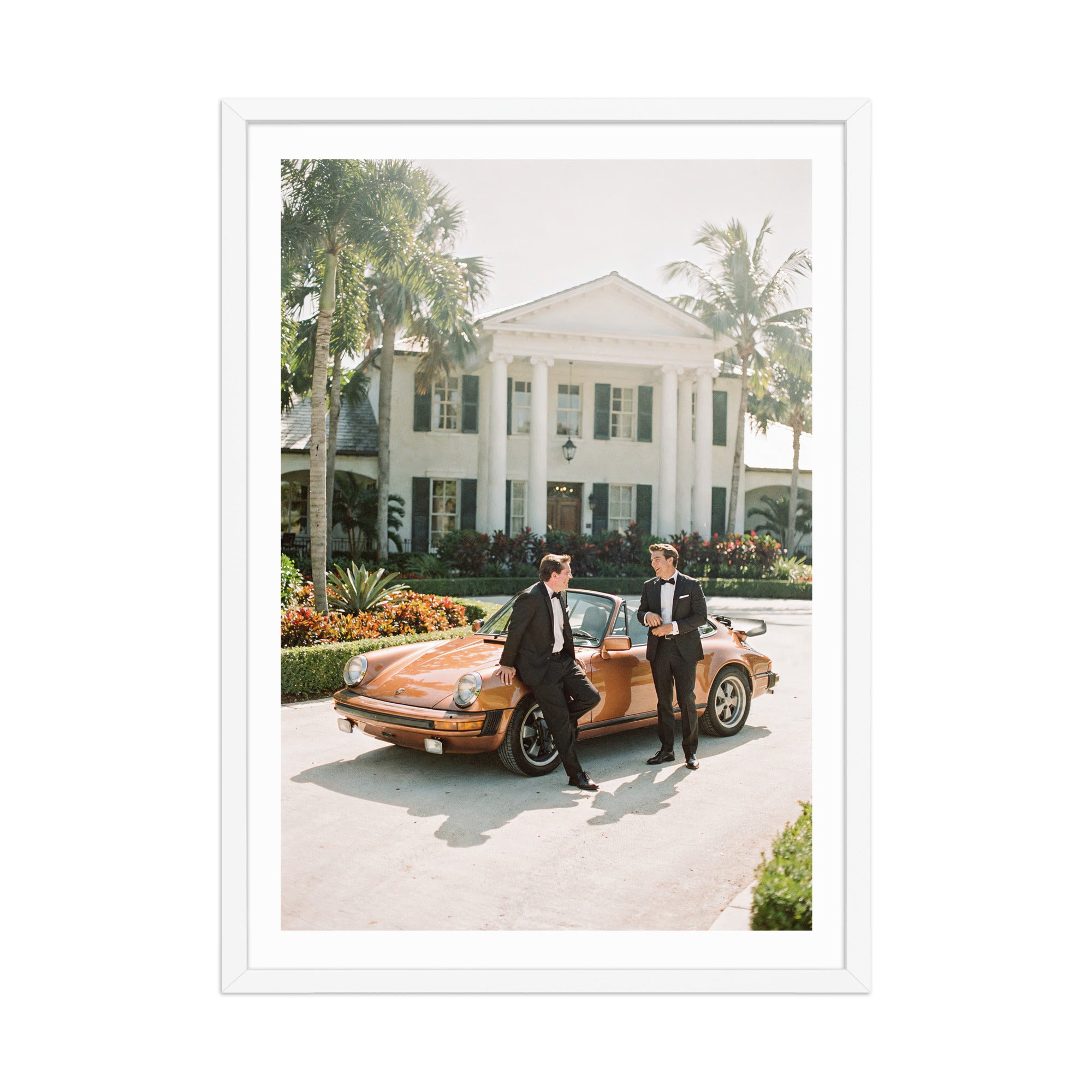 Two men in formal attire standing next to a vintage car in front of a large house with columns.