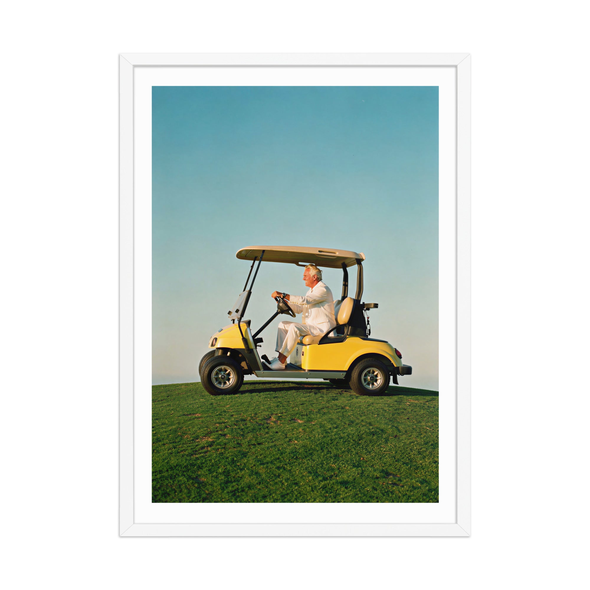 Man driving a yellow golf cart on a grassy field with a clear blue sky.
