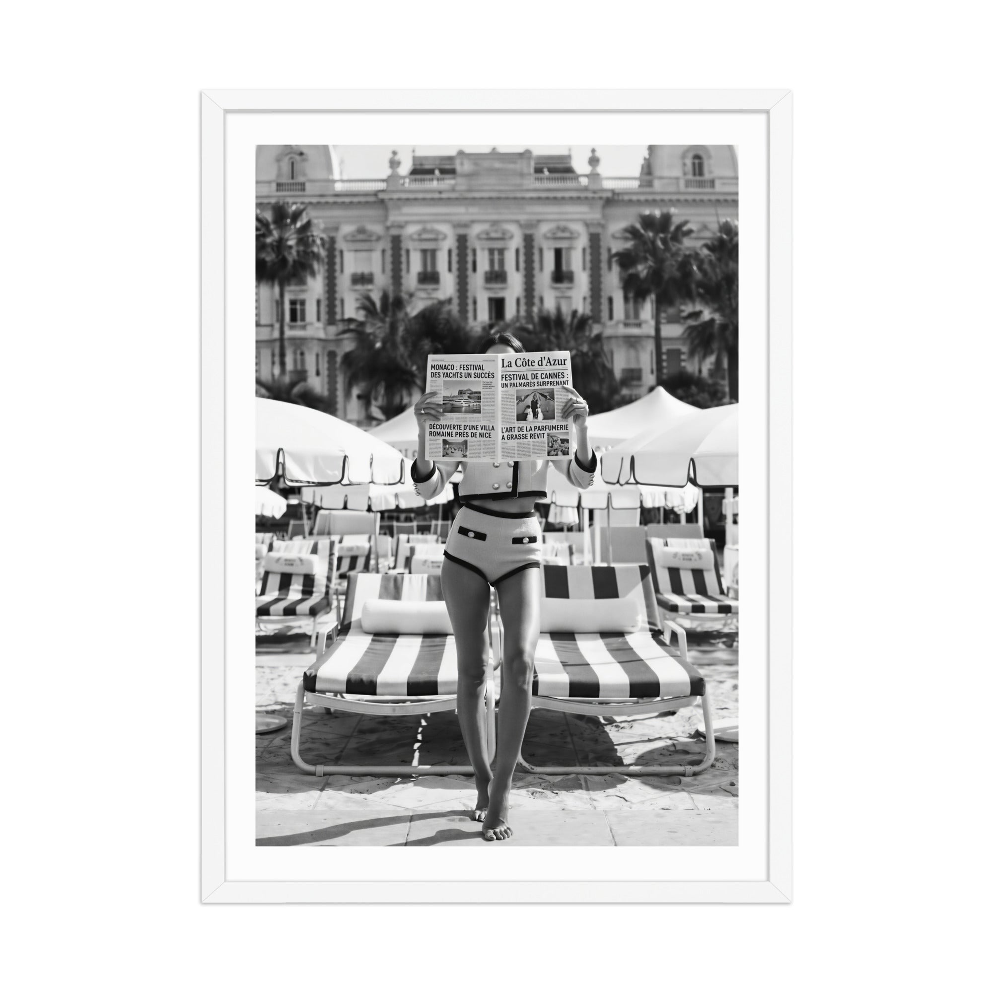 Person in vintage swimwear reading a newspaper on a striped chair with a building and palm trees in the background.